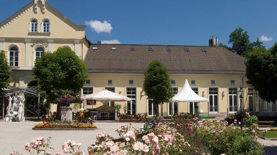 Ein schönes Gebäude mit einem blauen Himmel im Hintergrund. Im Vordergrund sind blühende Rosen und Bäume zu sehen. | © TVB Ausseerland - Salzkammergut_Rast