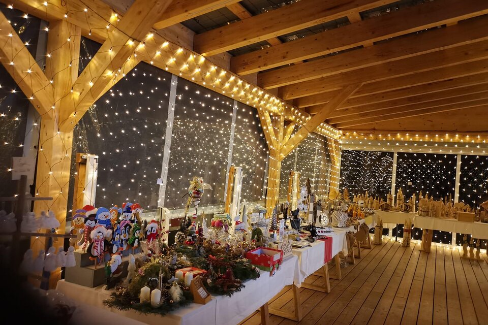 Ein festlich dekorierter Raum mit vielen Lichtern und einer Holzstruktur. Auf den Tischen sind verschiedene handgefertigte Weihnachtsartikel ausgestellt. | © Flourl´s Schenke