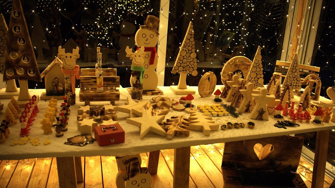 Ein Tisch mit handgemachten Weihnachtsdekorationen aus Holz. Im Hintergrund funkeln Lichter und schaffen eine festliche Atmosphäre. | © Flourl´s Schenke