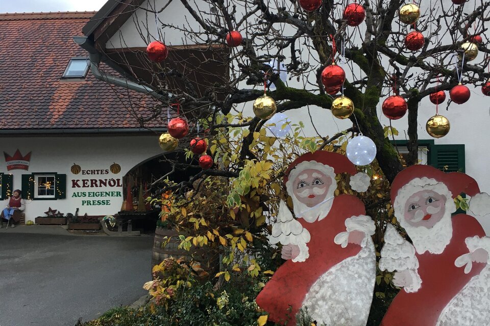 Ein festlich dekorierter Hof mit einem geschmückten Baum. Zwei große Weihnachtsmann-Figuren stehen im Vordergrund. | © Farmer-Rabensteiner