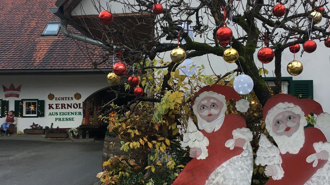 Ein festlich dekorierter Hof mit einem geschmückten Baum. Zwei große Weihnachtsmann-Figuren stehen im Vordergrund. | © Farmer-Rabensteiner