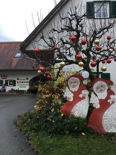 A festively decorated courtyard with a adorned tree. Two large Santa Claus figures stand in the foreground. | © Farmer-Rabensteiner