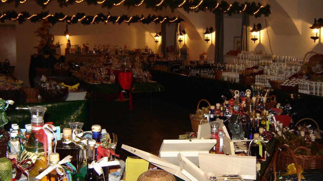 Ein festlich dekorierter Raum mit vielen Tischen, die mit traditionellen Geschenken und Delikatessen gedeckt sind. Die Wände sind mit Lichtern und grünen Pflanzen geschmückt. | © Farmer-Rabensteiner vlg. GRAF