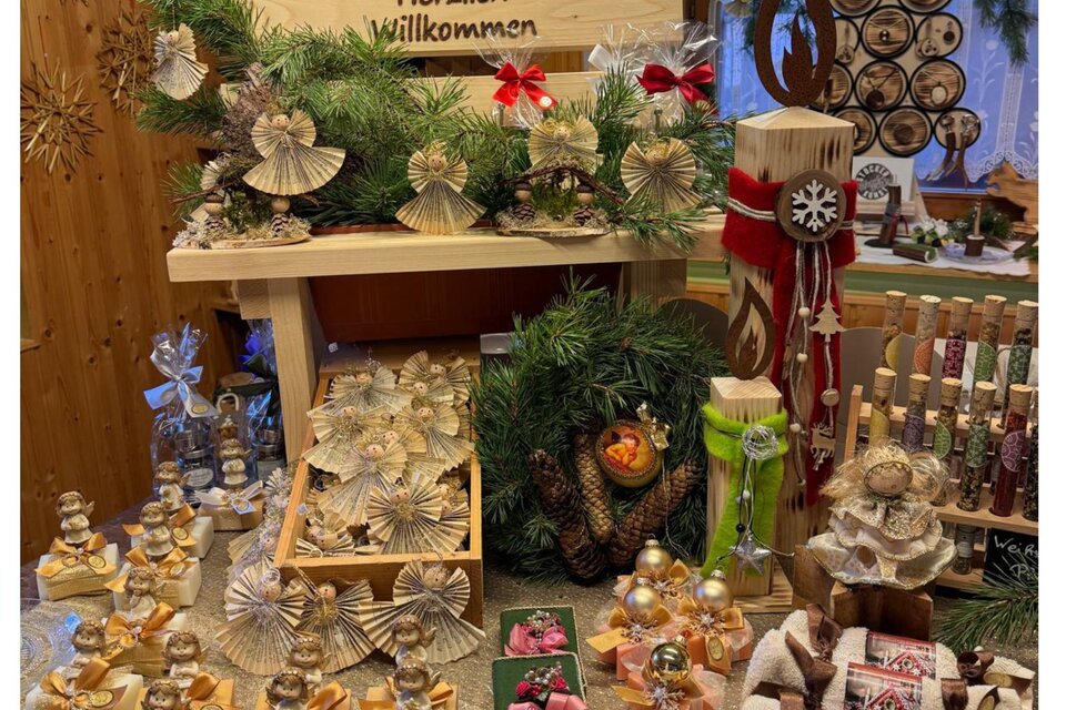 Ein festlich dekorierter Tisch mit handgemachten Weihnachtsgeschenken und -dekorationen. Im Hintergrund steht ein Begrüßungsschild mit der Aufschrift "Herzlich willkommen". | © Bauernladen Gröbming