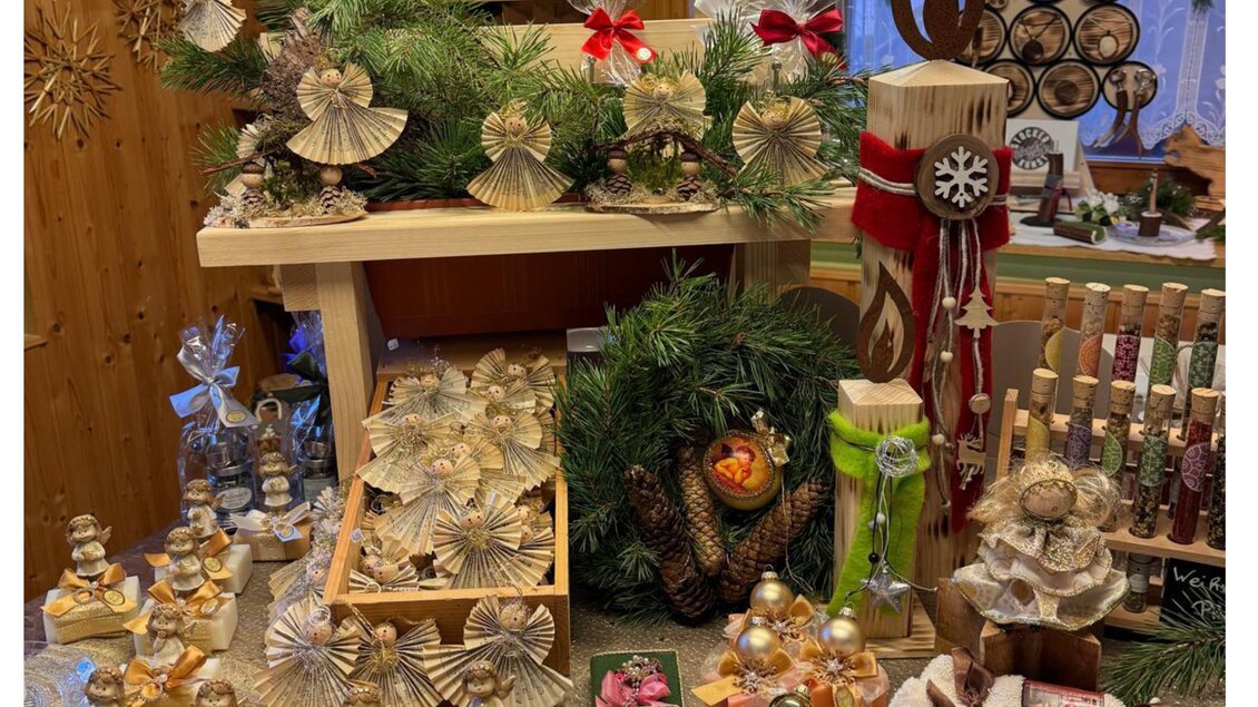 Ein festlich dekorierter Tisch mit handgemachten Weihnachtsgeschenken und -dekorationen. Im Hintergrund steht ein Begrüßungsschild mit der Aufschrift "Herzlich willkommen". | © Bauernladen Gröbming