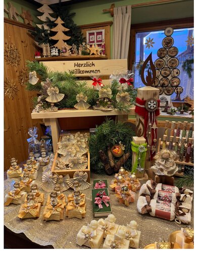 Ein festlich dekorierter Tisch mit handgemachten Weihnachtsgeschenken und -dekorationen. Im Hintergrund steht ein Begrüßungsschild mit der Aufschrift "Herzlich willkommen". | © Bauernladen Gröbming