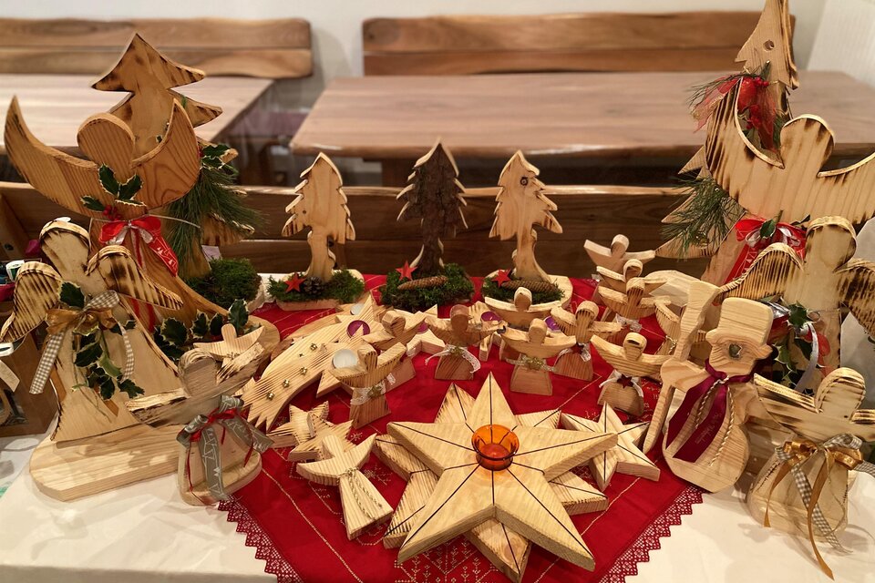 Eine festliche Holzkrippe mit geschnitzten Figuren und Bäumen auf einem roten Tuch. Die handgefertigten Dekorationen strahlen weihnachtliche Gemütlichkeit aus. | © Hofladen Hauptmann