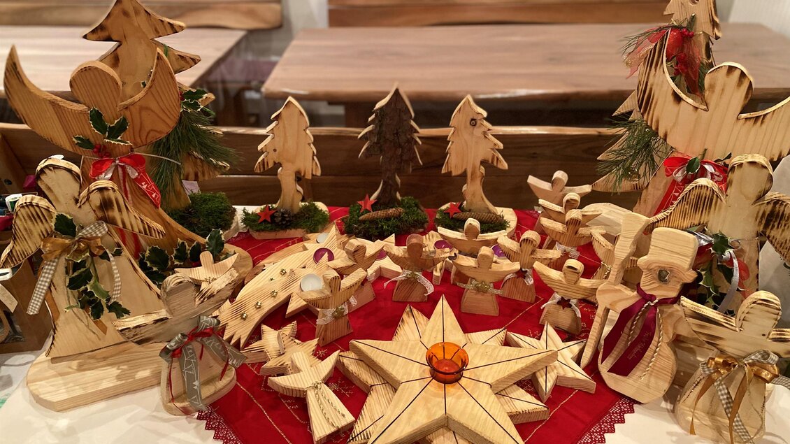 Eine festliche Holzkrippe mit geschnitzten Figuren und Bäumen auf einem roten Tuch. Die handgefertigten Dekorationen strahlen weihnachtliche Gemütlichkeit aus. | © Hofladen Hauptmann