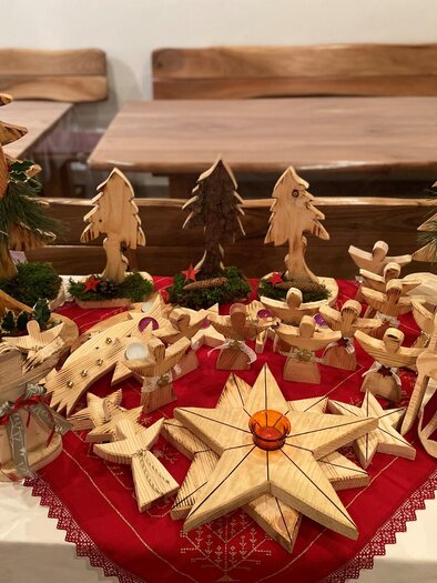 Eine festliche Holzkrippe mit geschnitzten Figuren und Bäumen auf einem roten Tuch. Die handgefertigten Dekorationen strahlen weihnachtliche Gemütlichkeit aus. | © Hofladen Hauptmann