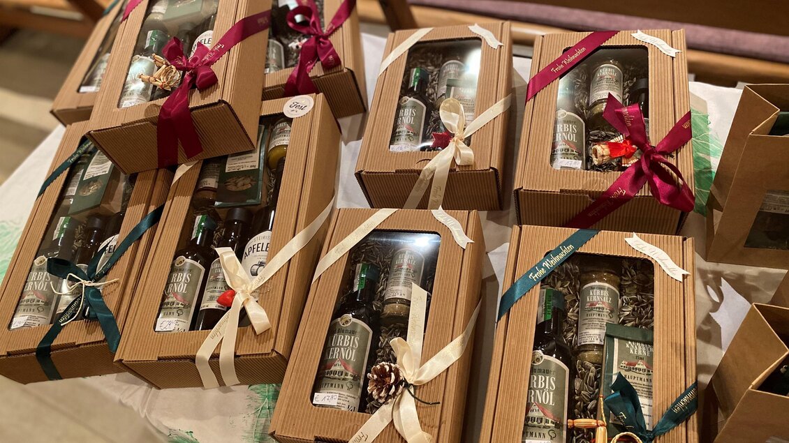 Mehrere Geschenkboxen mit Flaschen in verschiedenen Verpackungen sind auf einem Tisch angeordnet. Jede Box ist mit einer dekorativen Schleife geschmückt. | © Hofladen Hauptmann