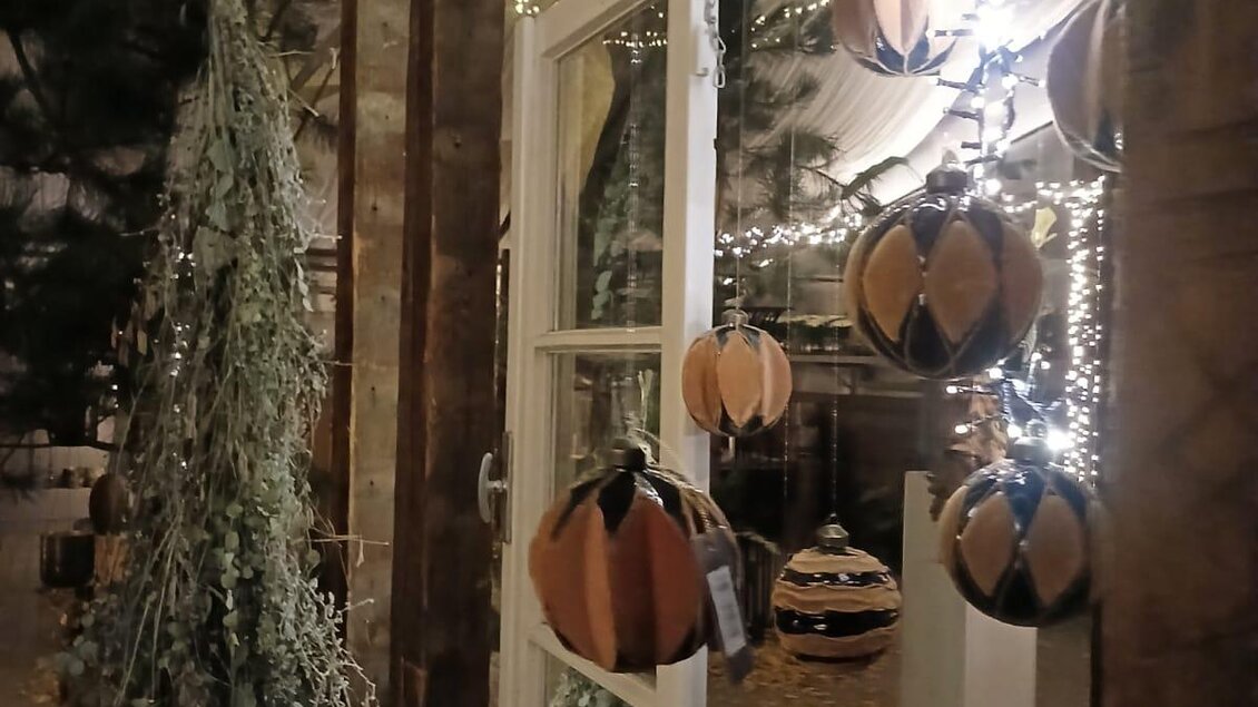 Ein gemütlicher Raum mit festlicher Dekoration und hängenden, bunten Ornamenten. Sanftes Licht strahlt von einer Lichterkette und sorgt für eine einladende Atmosphäre.