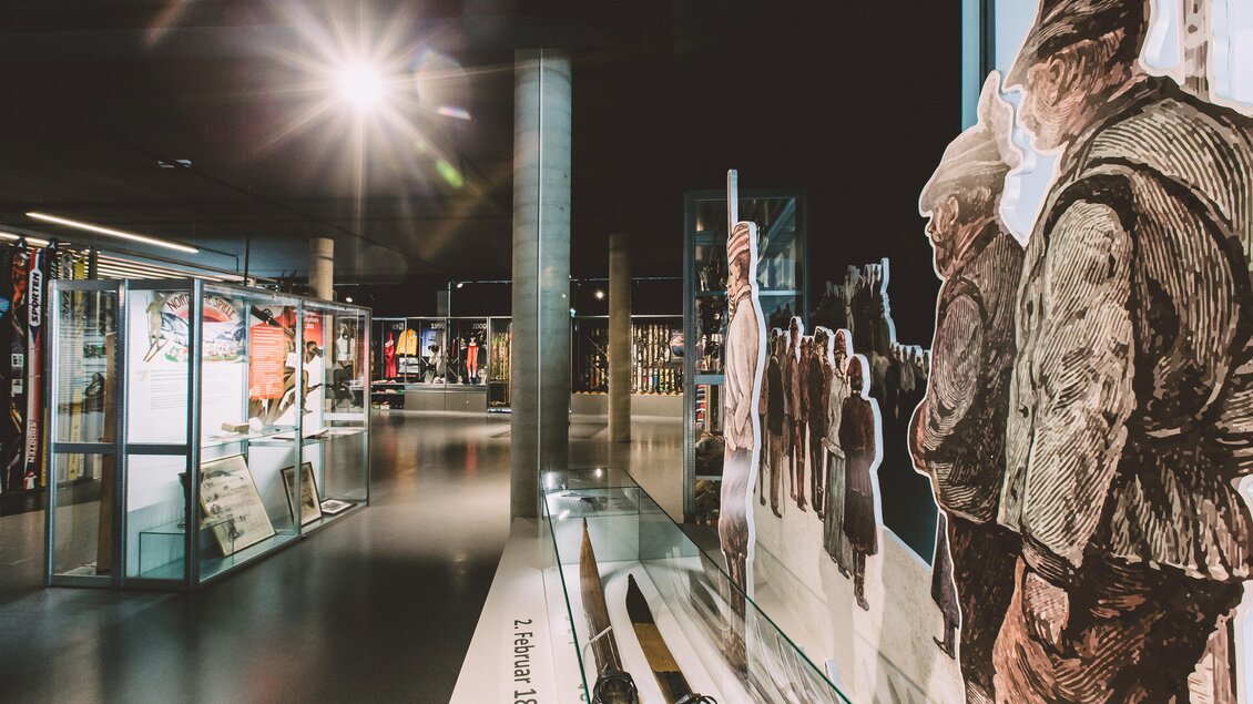 Ein moderner Ausstellungsraum mit interaktiven Vitrinen und historischen Illustrationen. Die Wände zeigen Menschen in traditioneller Kleidung und kunstvolle Exponate. | © nicoleseiser.at