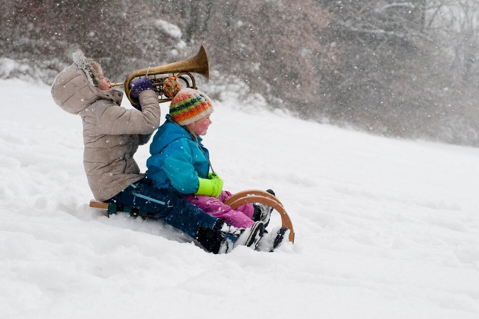 Zwei Kinder spielen im Schnee. Eines sitzt auf einem Schlitten, während das andere auf einem Horn bläst. | © Martina Unterrainer