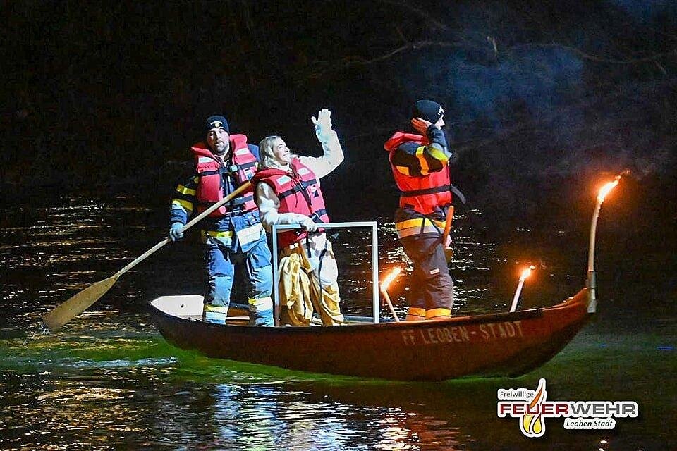 Drei Personen in Rettungswesten fahren in einem Boot auf dem Wasser. Sie halten Fackeln in der Hand und sind bei Nacht unterwegs. | ©  FF Leoben-Stadt