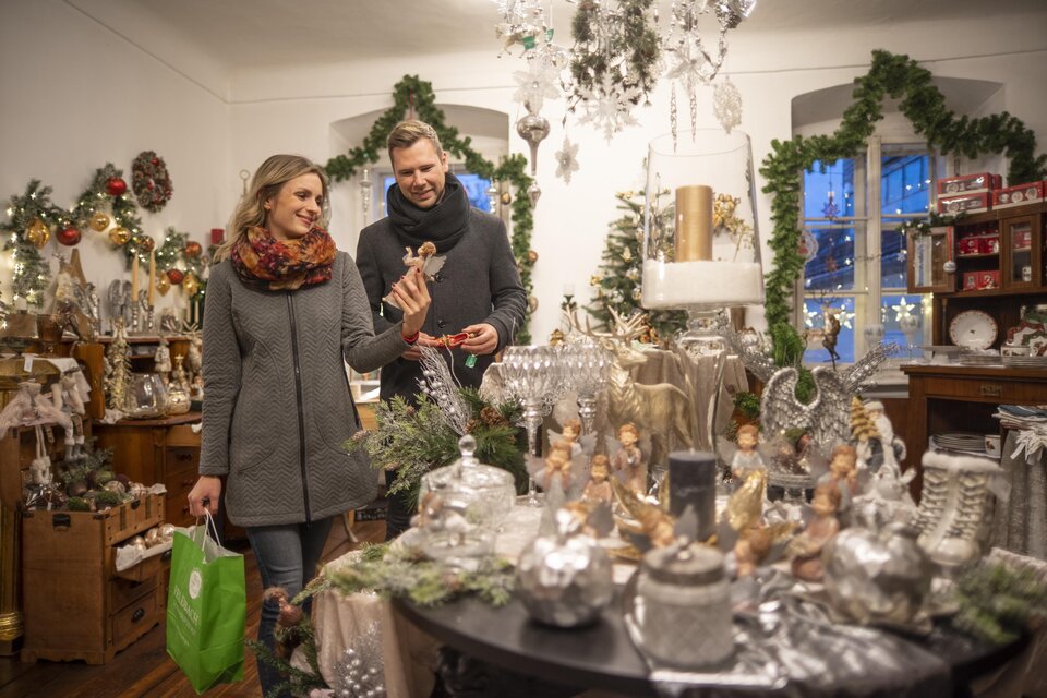 Ein gemütlicher Laden mit festlicher Weihnachtsdekoration. Ein Paar schaut sich Geschenke und Dekorationen an. | © Stadtgemeinde Feldbach I Bernhard Bergmann