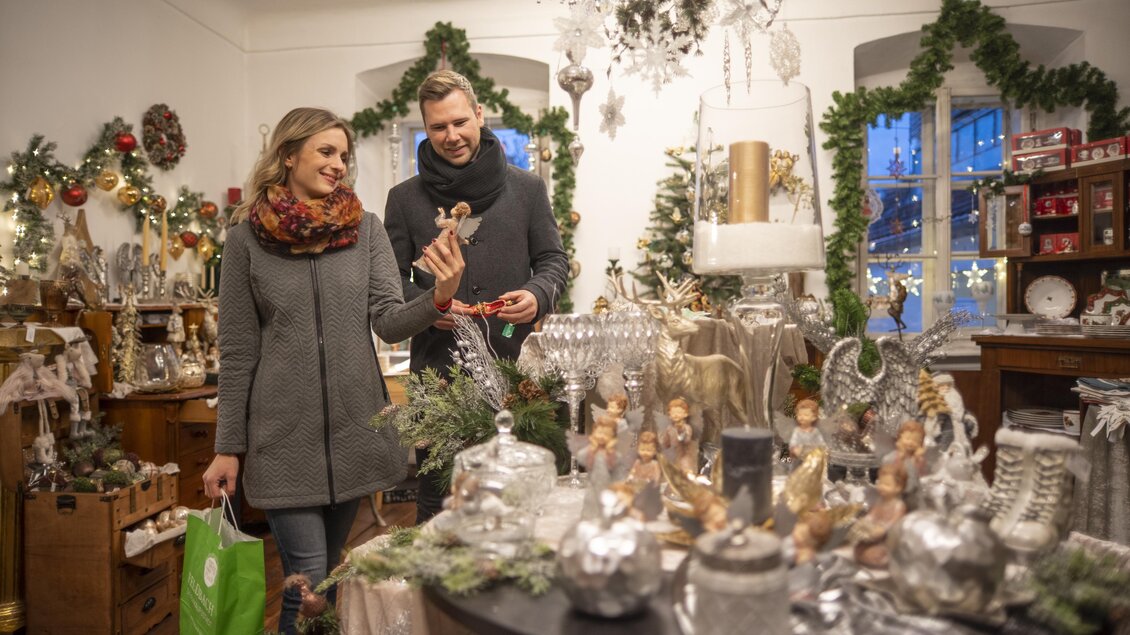 Ein gemütlicher Laden mit festlicher Weihnachtsdekoration. Ein Paar schaut sich Geschenke und Dekorationen an. | © Stadtgemeinde Feldbach I Bernhard Bergmann