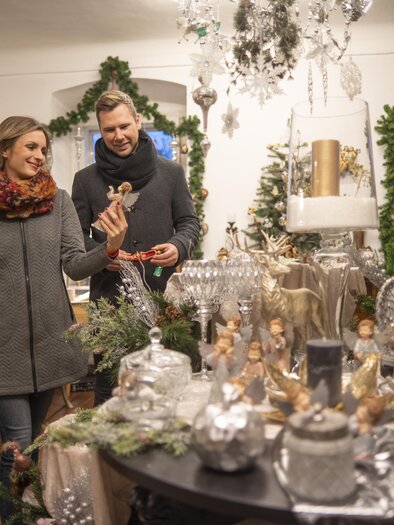 A cozy store with festive Christmas decorations. A couple is looking at gifts and decorations. | © Stadtgemeinde Feldbach I Bernhard Bergmann