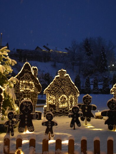 A festive winter landscape with glowing gingerbread houses and figurine gingerbread figures. The snow creates a magical, wintry atmosphere. | © Fam. Zwanzleitner