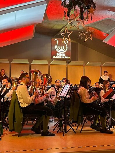 A wind orchestra is playing on stage. The room is festively decorated with decorations and colorful lights. | © Marktmusikkapelle St. Anna/A.