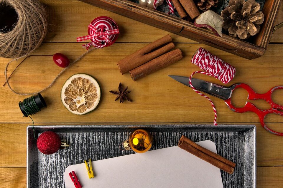 Eine rustikale Anordnung von Weihnachtsdekorationen, einschließlich Trockenfrüchte, Zimtstangen und Kugeln. Ein leerer Zettel liegt bereit für persönliche Nachrichten oder gute Wünsche. | © Pixabay