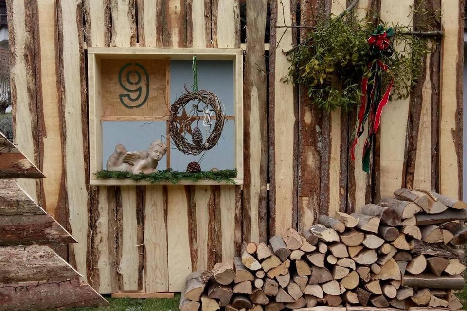 Eine rustikale Wand aus Holz mit einer dekorativen Nische. Darin befindet sich ein Kranz und ein kleiner Weihnachtsmann aus Holz, neben einem Holzstapel. | © Rudolf Kainz