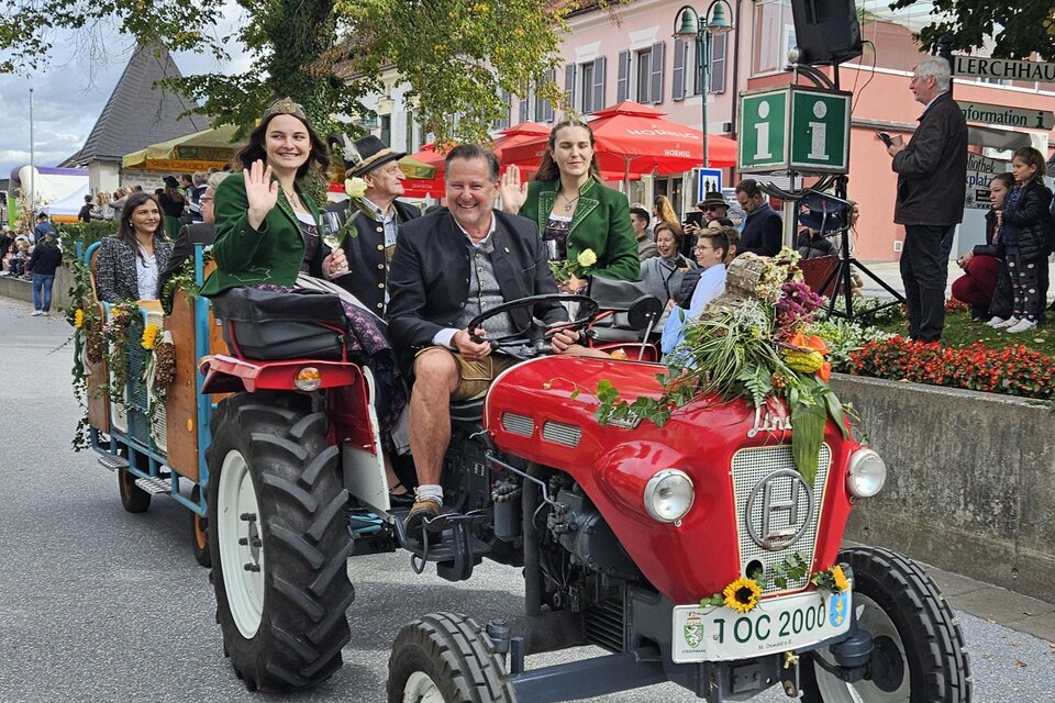 Eine festliche Parade mit einem roten Traktor, auf dem Personen in traditioneller Kleidung sitzen. Die Wagen sind mit Blumen dekoriert und ziehen viele Zuschauer an. | © Gemeinde Eibiswald