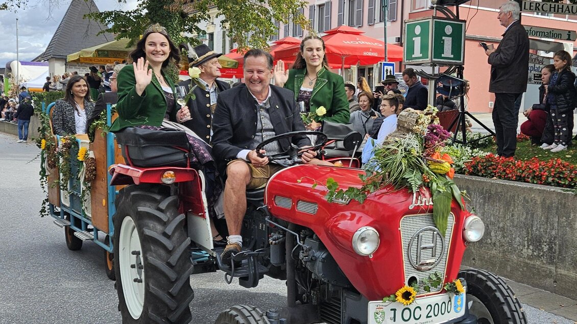 Eine festliche Parade mit einem roten Traktor, auf dem Personen in traditioneller Kleidung sitzen. Die Wagen sind mit Blumen dekoriert und ziehen viele Zuschauer an. | © Gemeinde Eibiswald
