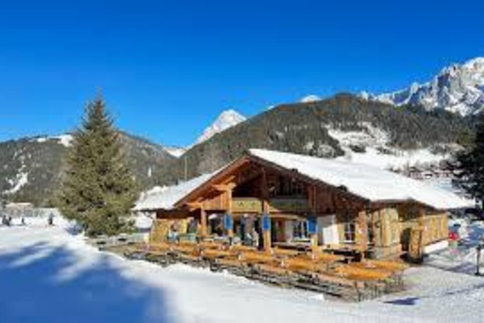 Ein schneebedecktes Bergdorf mit einer gemütlichen, rustikalen Hütte. Der klare blaue Himmel und die umliegenden Berge schaffen eine schöne Winterlandschaft. | © Waldcafe Liftstüberl
