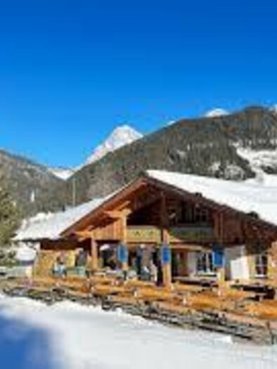 Ein schneebedecktes Bergdorf mit einer gemütlichen, rustikalen Hütte. Der klare blaue Himmel und die umliegenden Berge schaffen eine schöne Winterlandschaft. | © Waldcafe Liftstüberl