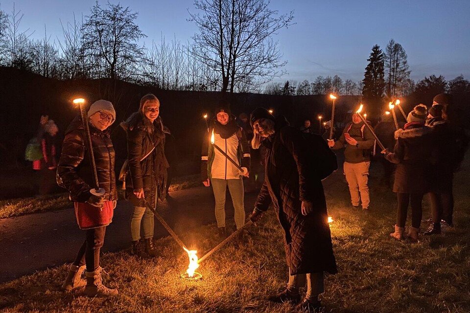 Eine Gruppe von Menschen steht im Dunkeln und hält Fackeln in den Händen. Sie sind umgeben von Bäumen und der Himmel ist dunkelblau. | © cdm - Claudia Dunst