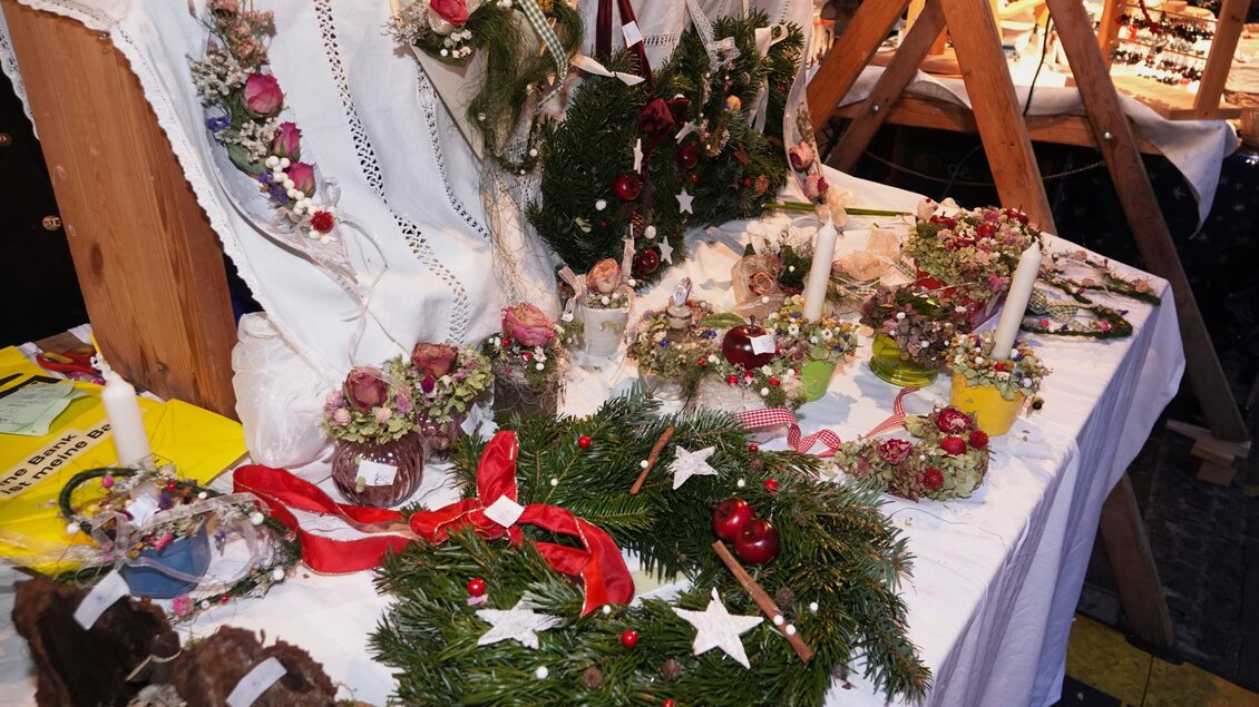 Ein Tisch mit festlich dekorierten Kränzen und Weihnachtsartikeln. Es sind Kerzen und blumige Verzierungen zu sehen.