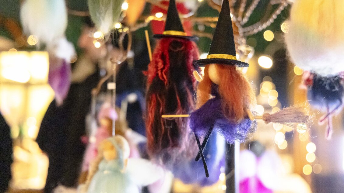 Bunte Figuren von kleinen Hexen und Feen hängen dekorativ an einem Ständer. Sie sind aus weichem Material und strahlen eine festliche Atmosphäre aus.