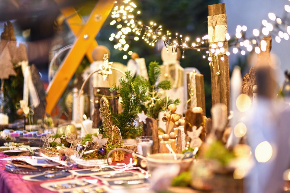 Ein festlich dekorierter Tisch mit handgemachten Kunstwerken und weihnachtlicher Beleuchtung. Die Atmosphäre ist warm und einladend, ideal für Weihnachtsmärkte. | © KK