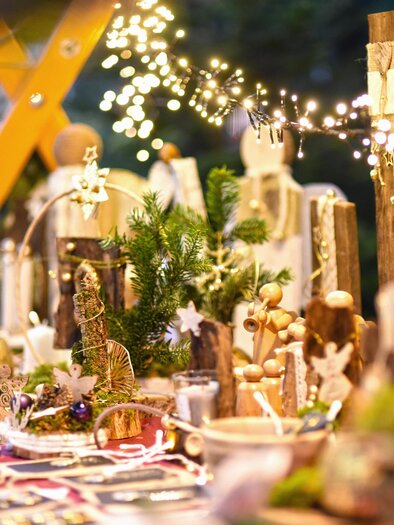 A festively decorated table with handmade artworks and Christmas lighting. The atmosphere is warm and welcoming, ideal for Christmas markets. | © KK