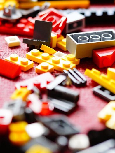 Colorful LEGO bricks are scattered on a table. The pieces come in various shapes and colors, mainly red, yellow, and black. | © pixabay