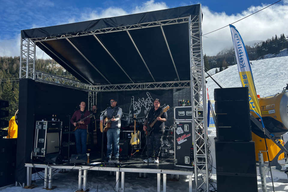 Eine Band spielt auf einer Bühne im Freien in einer schneebedeckten Landschaft. Im Hintergrund sind Bäume und ein blauer Himmel zu sehen. | © Hauser Kaibling