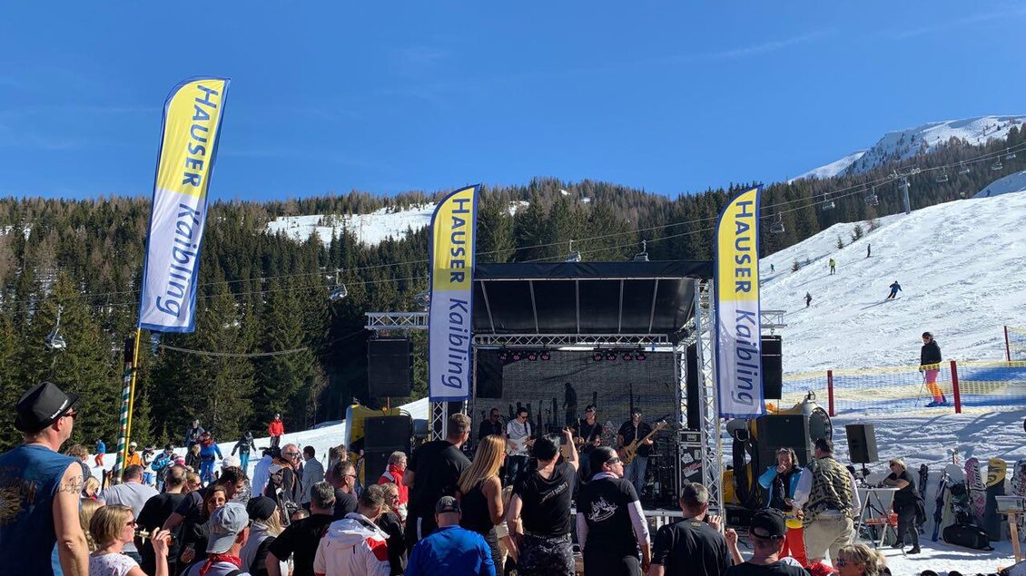 Eine lebhafte Veranstaltung auf einem Schneegebiet mit vielen Menschen. Im Hintergrund ein Bühnenaufbau und klare, sonnige Himmel. | © Hauser Kaibling