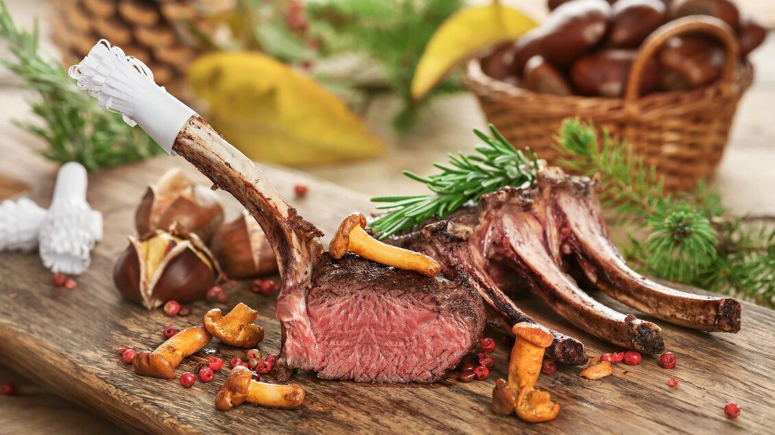 Ein köstliches Lammkarree, perfekt zubereitet, liegt auf einem Holzteller. Darum liegen frische Pfifferlinge und rosafarbene Pfefferkörner. | © Foto Fotolia