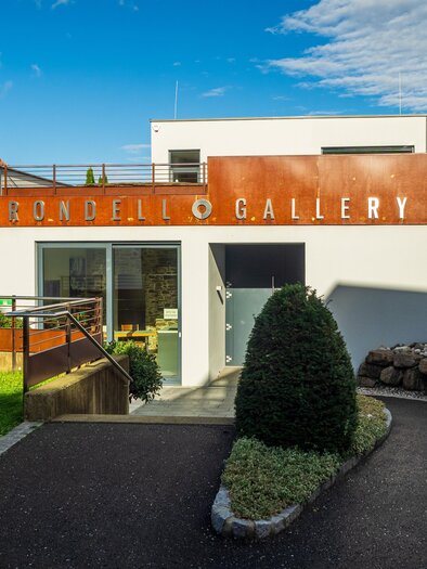 A modern gallery building with the inscription "Rondell Gallery". Surrounded by a well-kept garden and a blue sky. | © TV Südsteiermark