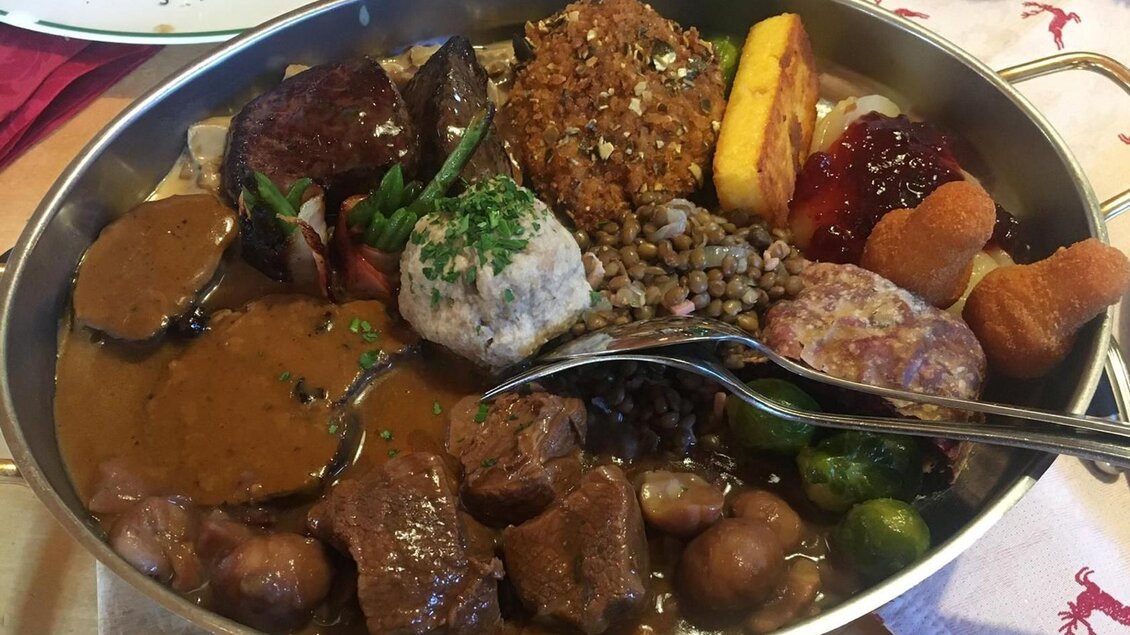 Ein großer Teller mit einer Auswahl an verschiedenen Fleischgerichten, Klößchen und Beilagen. Das Gericht ist reichhaltig und farbenfroh präsentiert. | © Tanja Kirchschlager