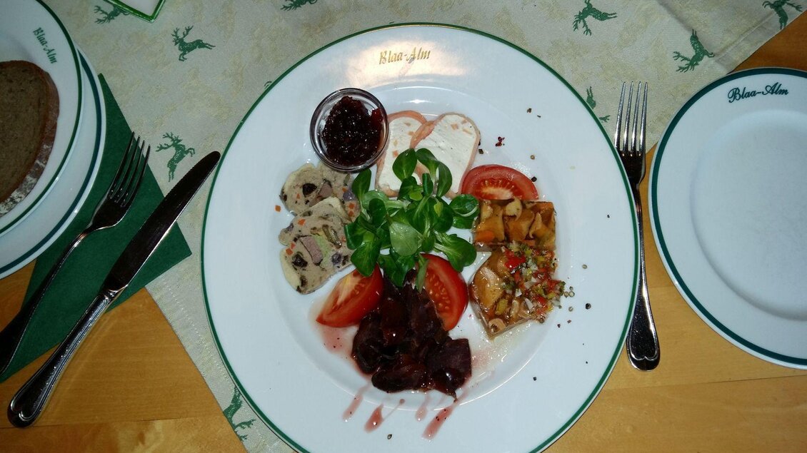 Ein Teller mit verschiedenen Gerichten, darunter Fleisch, Tomaten und frische Kräuter. Dazu ein Schälchen mit einer Sauce. | © Petra Kirchschlager