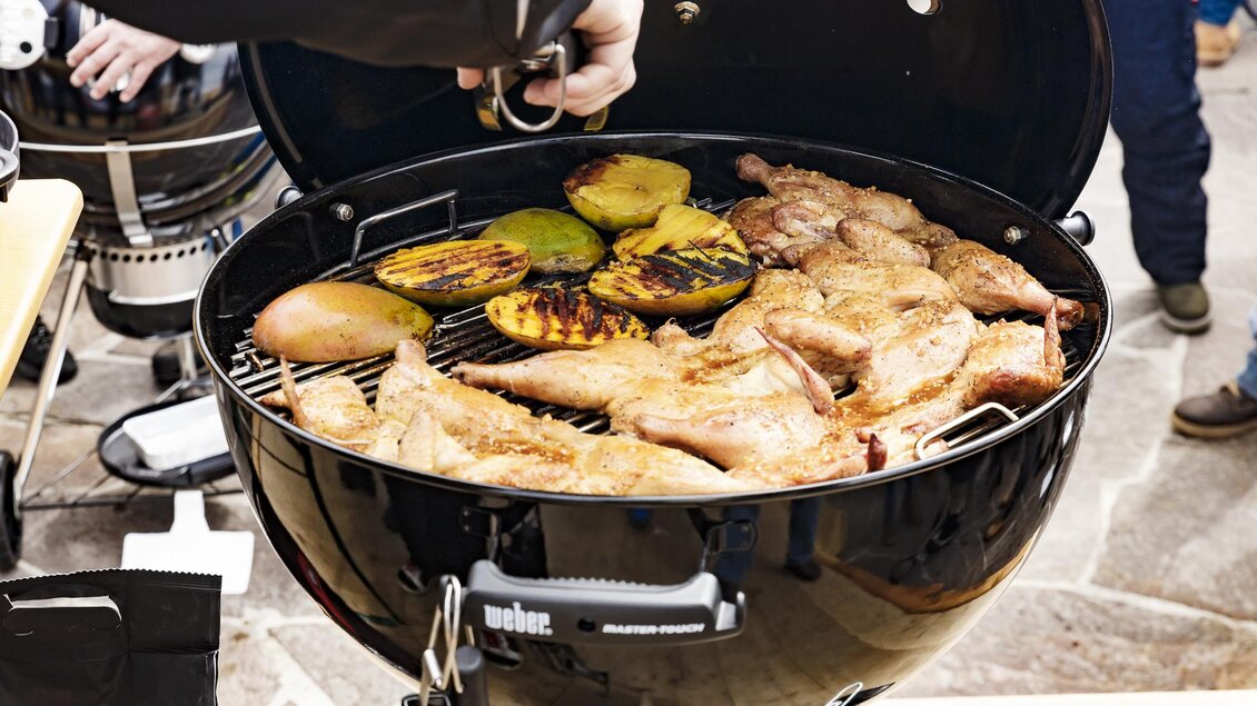 Ein Grill mit gegrilltem Hähnchen und Gemüse. Der Grill ist schwarz und steht auf einem Tisch im Freien. | © Christoph Buchegger