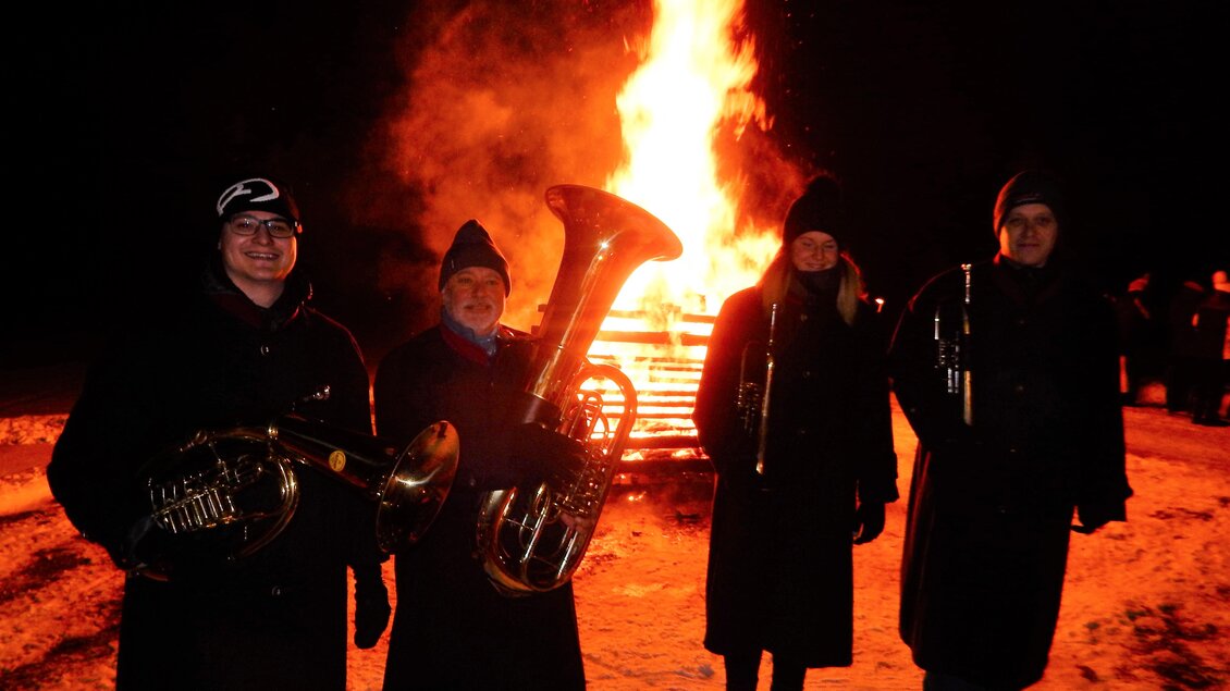 Eine Gruppe von vier Menschen steht im Schnee vor einem großen Feuer. Sie halten Musikinstrumente und tragen warme Kleidung. | © Gemeinde Mitterberg-St. Martin