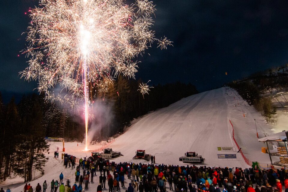 Ein beeindruckendes Feuerwerk leuchtet über einer verschneiten Piste. Viele Menschen stehen zusammen und genießen das festliche Spektakel. | © Michael Simonlehner
