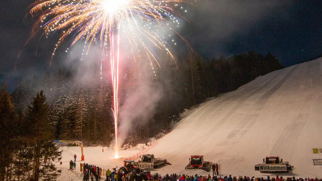 Ein großes Feuerwerk leuchtet über einer Menschenmenge im Schnee. Die Szene ist lebhaft und festlich, mit vielen Besuchern, die das Spektakel genießen. | © Michael Simonlehner