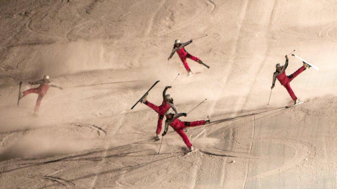 Mehrere Skifahrer zeigen akrobatische Sprünge auf einer schneebedeckten Piste. Die Skifahrer tragen rote Outfits und hinterlassen Spuren im Schnee. | © Michael Simonlehner