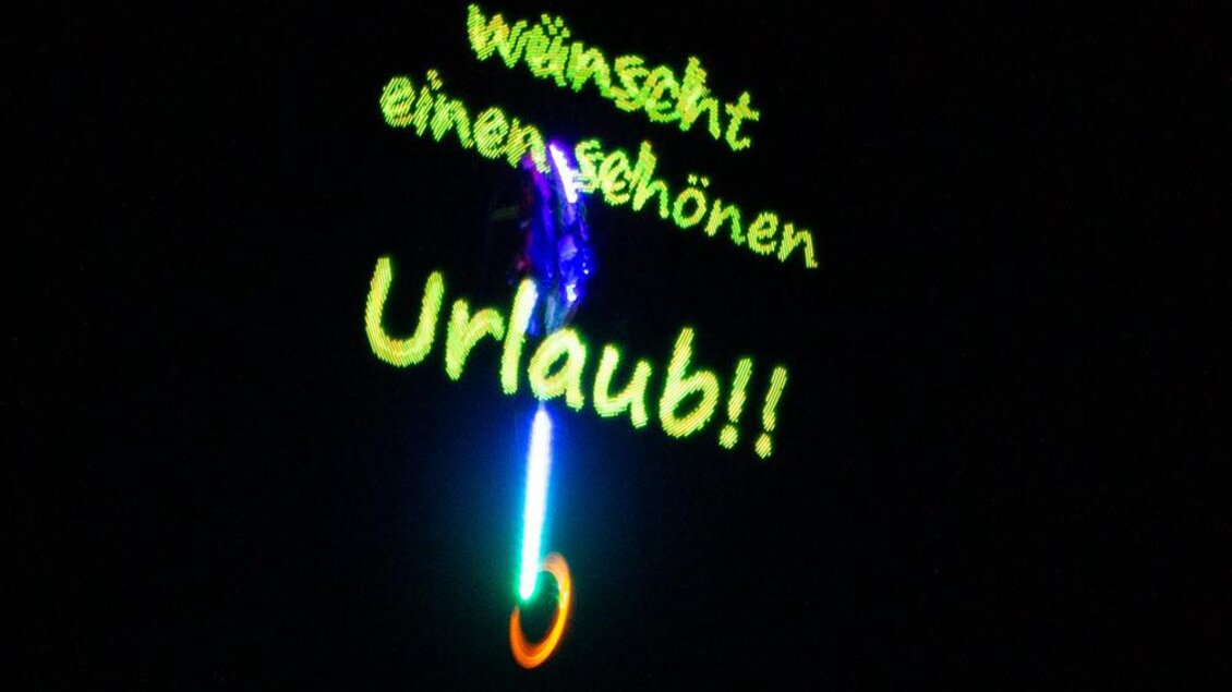 Ein bunter Schriftzug leuchtet im Dunkeln und wünscht einen schönen Urlaub. Die Farben sind lebhaft und ziehen die Aufmerksamkeit auf sich. | © Michael Simonlehner