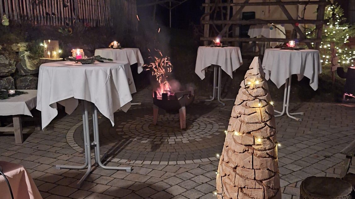 Ein festlich dekorierter Außenbereich mit Tischen und Kerzen. Im Hintergrund steht ein geschmückter Weihnachtsbaum aus Holz. | © Bäuerinnen Weinitzen