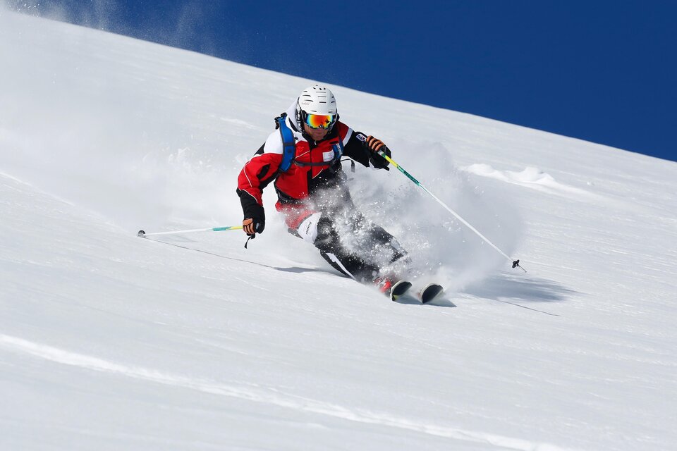 Ein Skifahrer fährt mit Schwung einen schneebedeckten Hang hinunter. Der klare blaue Himmel sorgt für ideale Bedingungen. | © Alpincenter