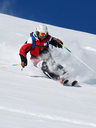 Ein Skifahrer fährt mit Schwung einen schneebedeckten Hang hinunter. Der klare blaue Himmel sorgt für ideale Bedingungen. | © Alpincenter